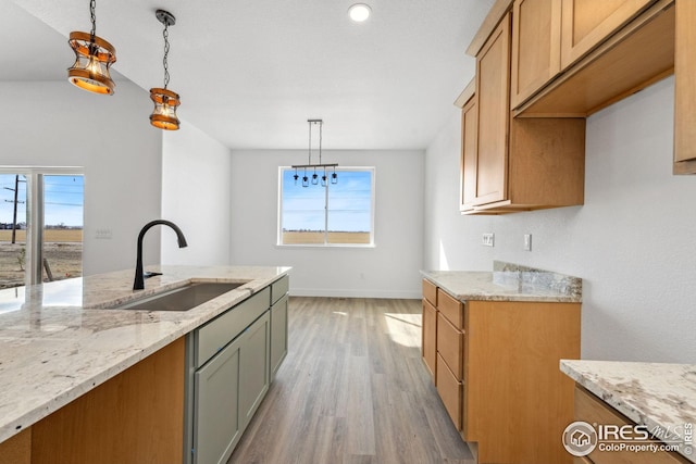 kitchen featuring pendant lighting, light stone countertops, light wood-type flooring, and a sink