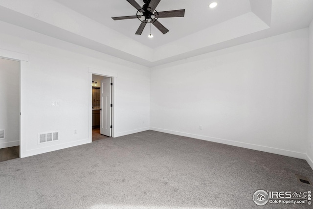 unfurnished bedroom with a tray ceiling, baseboards, visible vents, and dark colored carpet