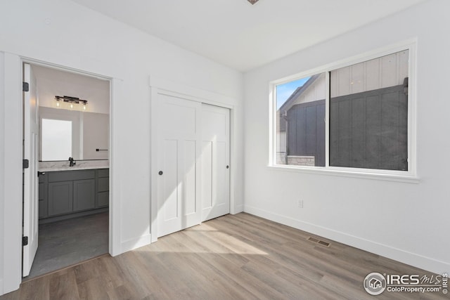 unfurnished bedroom with wood finished floors, visible vents, baseboards, a closet, and ensuite bathroom