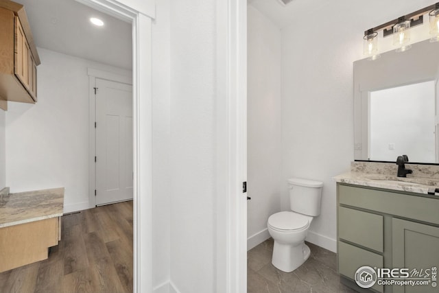 bathroom featuring toilet, vanity, baseboards, and wood finished floors