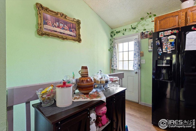 kitchen featuring vaulted ceiling, a textured ceiling, light wood-type flooring, and black refrigerator with ice dispenser