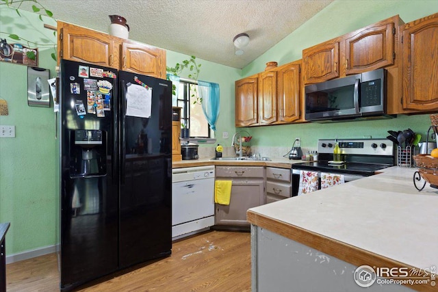 kitchen featuring sink, light hardwood / wood-style floors, vaulted ceiling, appliances with stainless steel finishes, and a textured ceiling