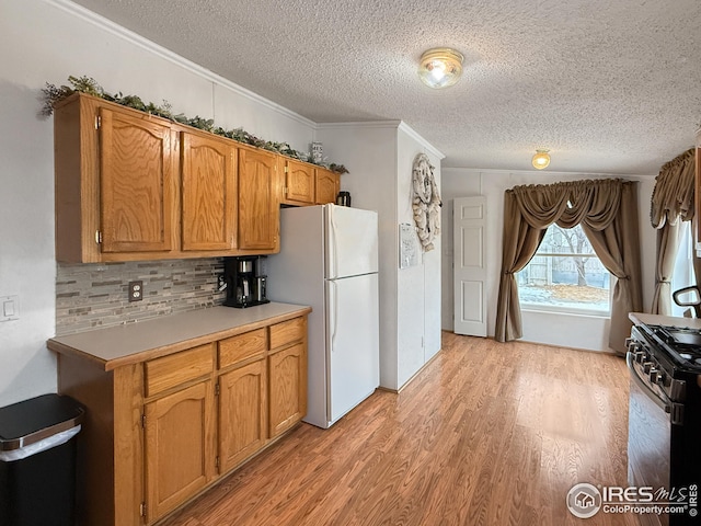 kitchen featuring brown cabinets, freestanding refrigerator, light countertops, light wood-style floors, and gas stove