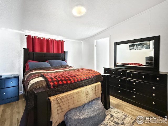 bedroom featuring lofted ceiling, a textured ceiling, and wood finished floors