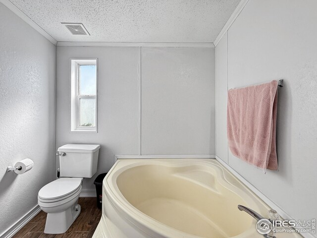 bathroom with visible vents, toilet, a textured ceiling, wood finished floors, and a bath