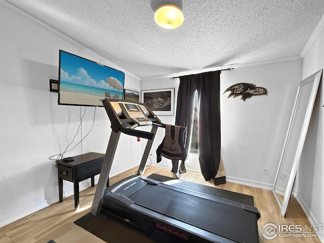 workout area featuring a textured ceiling, ornamental molding, wood finished floors, and baseboards