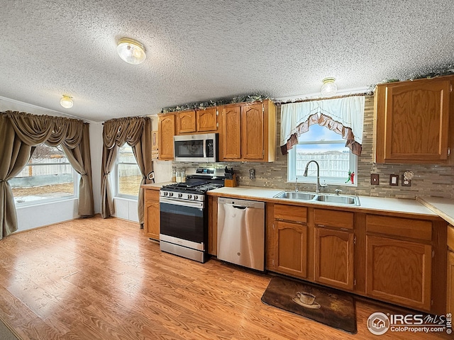 kitchen featuring stainless steel appliances, a sink, light wood-style floors, light countertops, and brown cabinetry