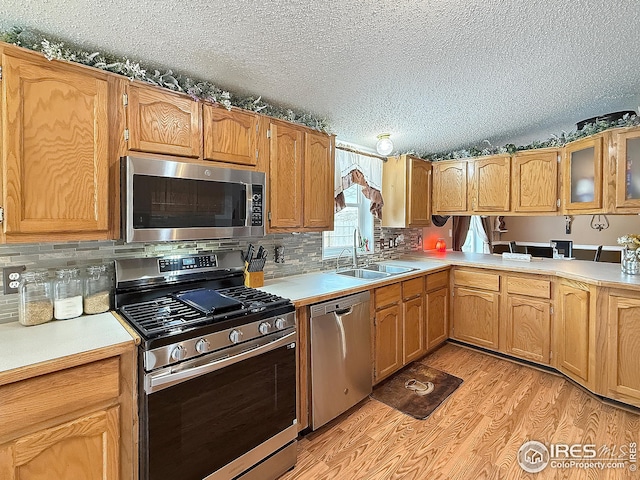 kitchen with a textured ceiling, a sink, light countertops, appliances with stainless steel finishes, and light wood-type flooring