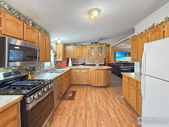 kitchen with light wood finished floors, appliances with stainless steel finishes, a sink, light countertops, and backsplash