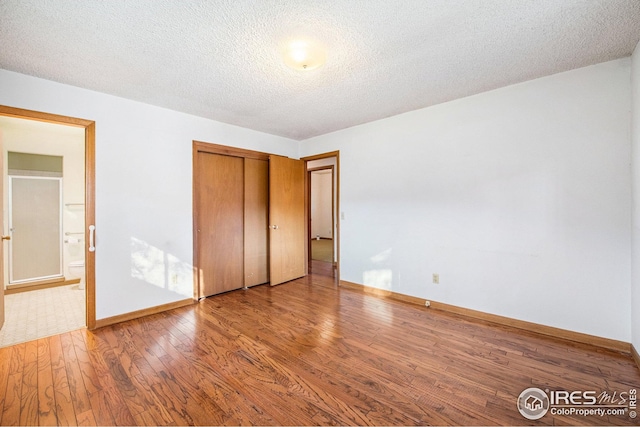 unfurnished bedroom featuring a textured ceiling, a closet, connected bathroom, and hardwood / wood-style floors