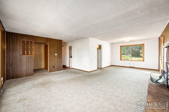 unfurnished living room featuring carpet, wooden walls, and a textured ceiling