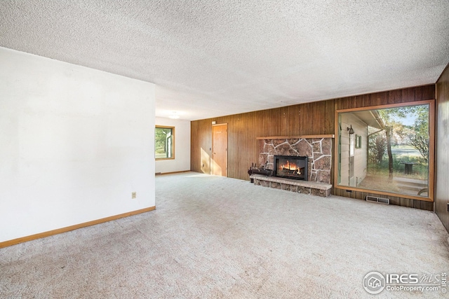 unfurnished living room featuring a textured ceiling, a fireplace, wood walls, and carpet flooring