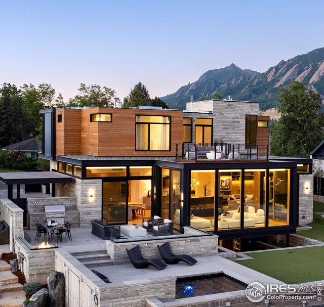 back house at dusk with an outdoor living space, a patio, a balcony, and a mountain view