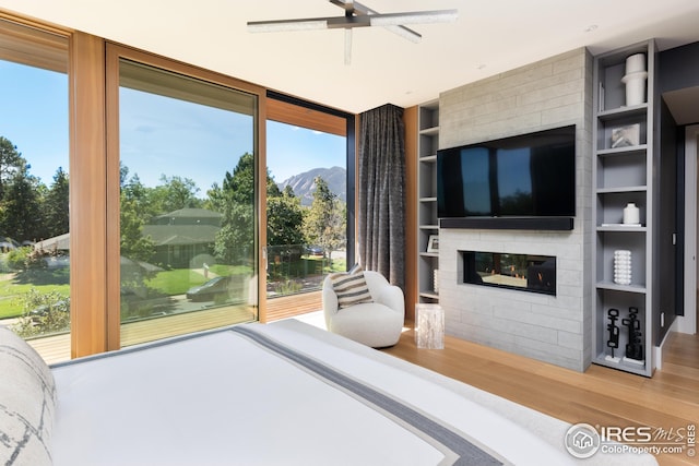 bedroom featuring hardwood / wood-style flooring, multiple windows, ceiling fan, and a large fireplace