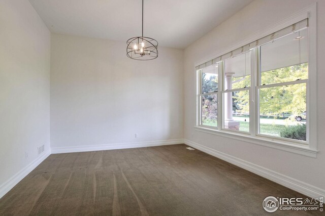 unfurnished room featuring an inviting chandelier and dark colored carpet