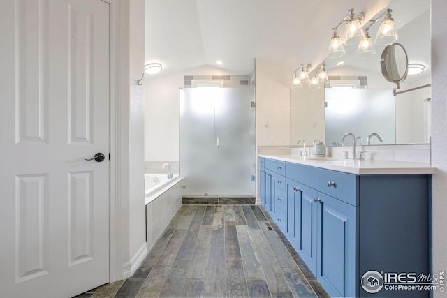 bathroom featuring vanity, wood-type flooring, tiled tub, and vaulted ceiling