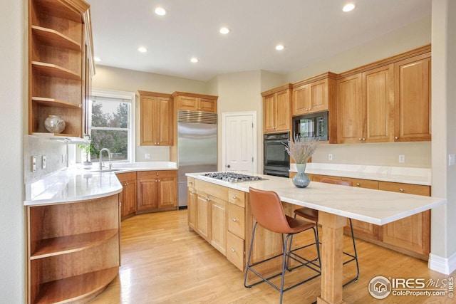 kitchen featuring light wood-type flooring, a breakfast bar, sink, black appliances, and a center island