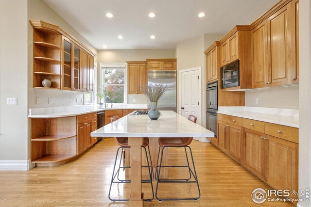 kitchen featuring sink, light hardwood / wood-style flooring, built in appliances, a breakfast bar area, and a kitchen island