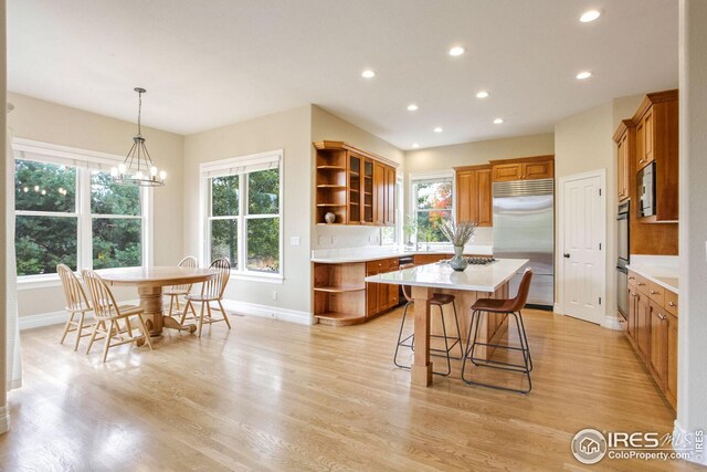 kitchen with a center island, hanging light fixtures, built in appliances, light wood-type flooring, and a kitchen bar