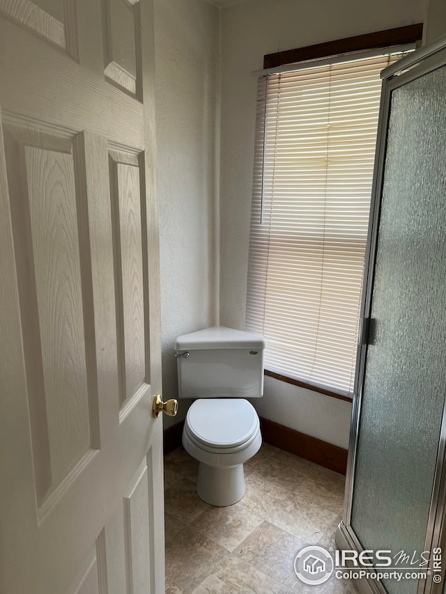 bathroom featuring a shower with door and toilet