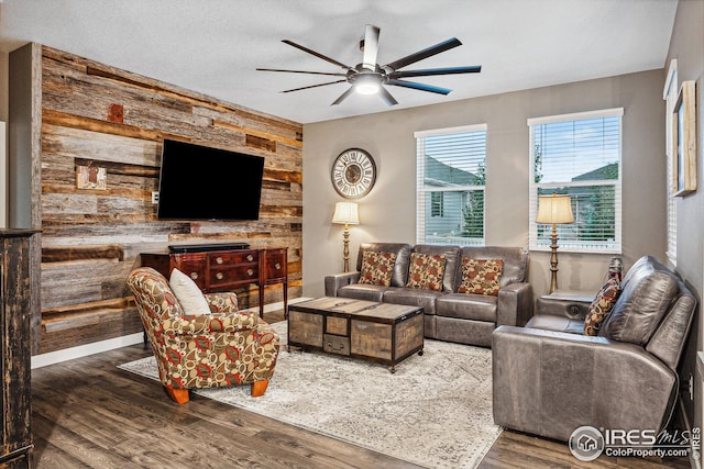 living room featuring a textured ceiling, dark wood-style flooring, wood walls, and a ceiling fan