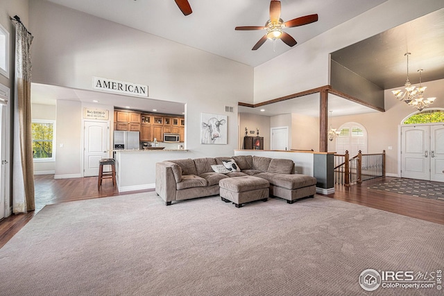 living room with ceiling fan with notable chandelier, a high ceiling, and dark hardwood / wood-style flooring