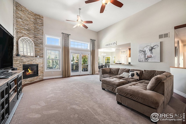 carpeted living room featuring a stone fireplace, a towering ceiling, and ceiling fan with notable chandelier