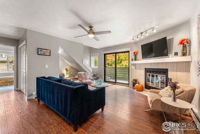 living area featuring stairway, hardwood / wood-style floors, a tile fireplace, a textured ceiling, and a ceiling fan