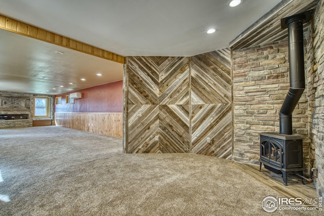 interior space with a wood stove, an AC wall unit, carpet flooring, and wooden walls