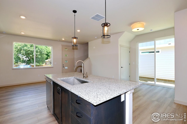 kitchen featuring sink, decorative light fixtures, light stone counters, light hardwood / wood-style flooring, and a center island with sink