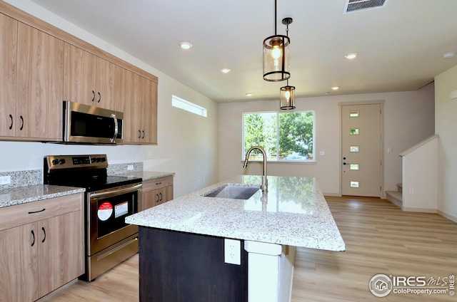 kitchen with appliances with stainless steel finishes, sink, pendant lighting, light hardwood / wood-style flooring, and a kitchen island with sink