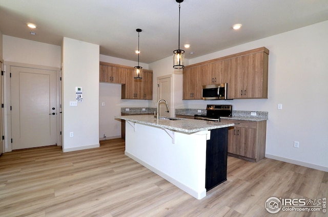 kitchen featuring sink, light wood-type flooring, stainless steel appliances, decorative light fixtures, and a kitchen island with sink