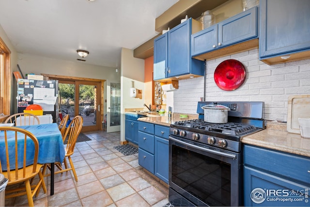 kitchen featuring blue cabinetry, decorative backsplash, gas range, stone finish floor, and light countertops