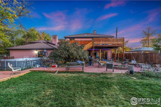 back of house at dusk featuring a chimney, fence, a deck, and a yard