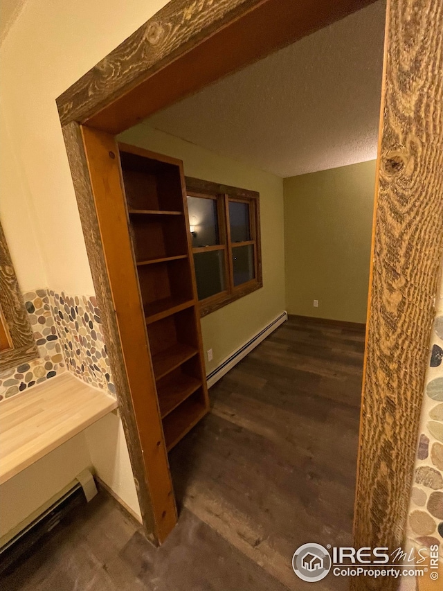 corridor featuring dark wood-type flooring, a baseboard heating unit, and a textured ceiling