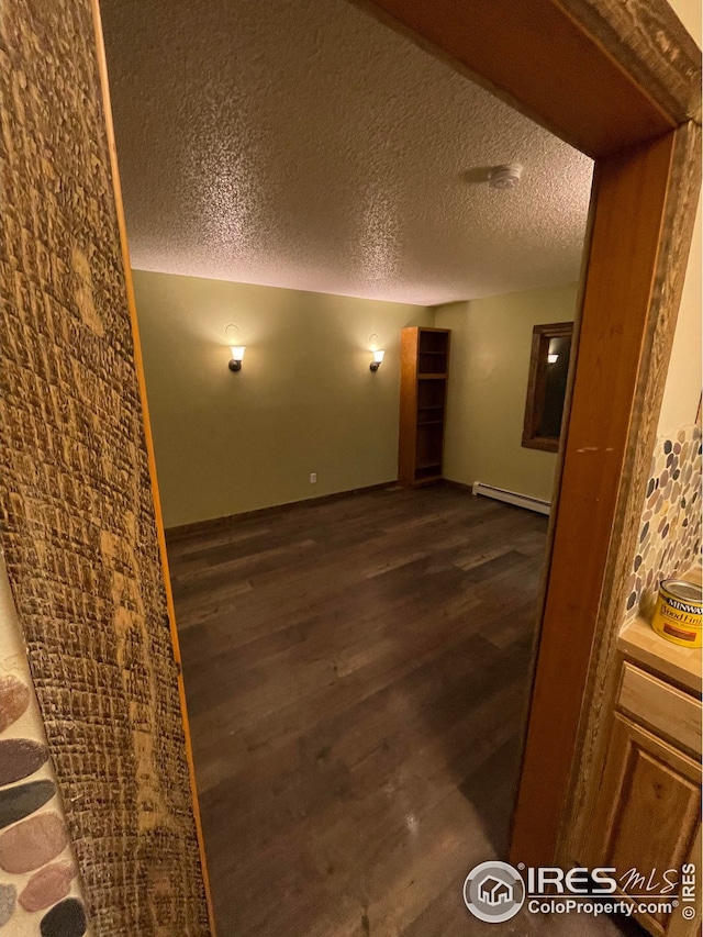 spare room with baseboard heating, dark wood-type flooring, and a textured ceiling