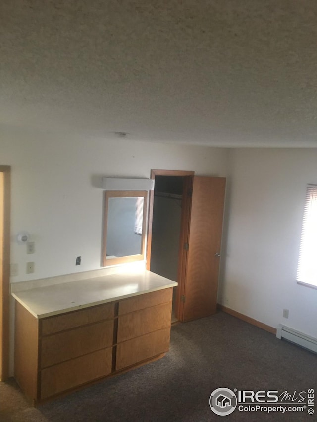 interior space with dark carpet, a baseboard heating unit, and a textured ceiling