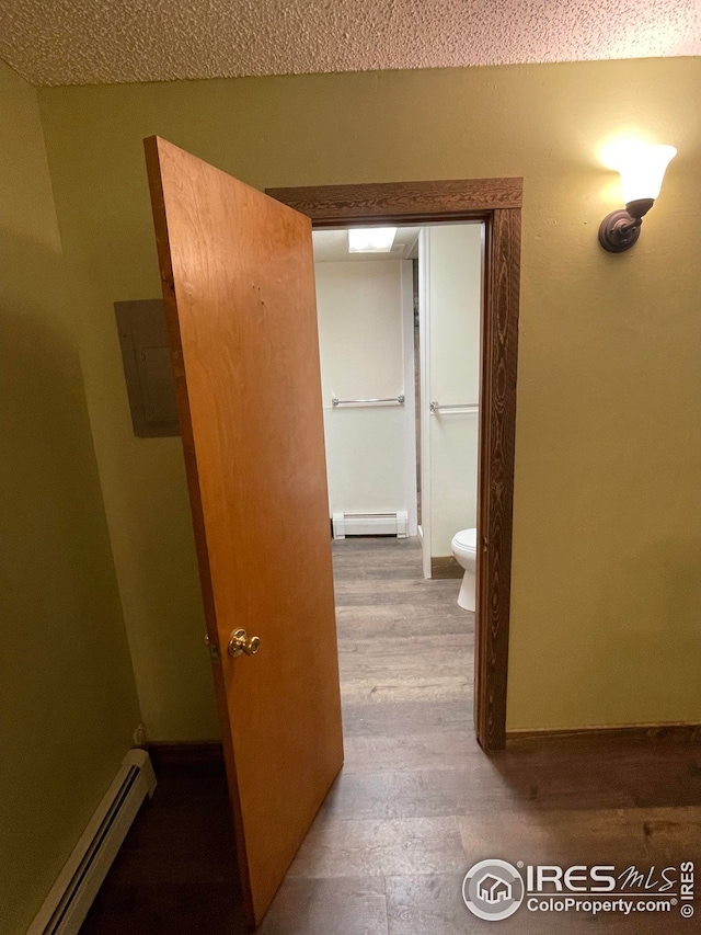 hall with light hardwood / wood-style floors, a textured ceiling, electric panel, and baseboard heating