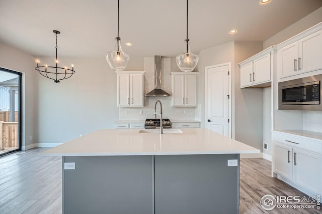 kitchen with wall chimney exhaust hood, white cabinets, decorative light fixtures, and a center island with sink