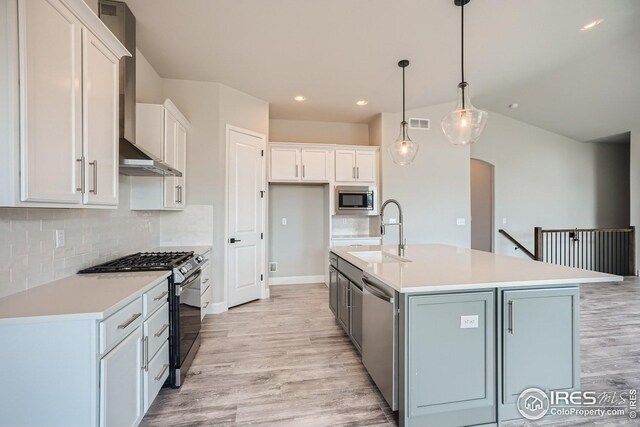 kitchen featuring white cabinets, a center island with sink, sink, decorative light fixtures, and stainless steel appliances