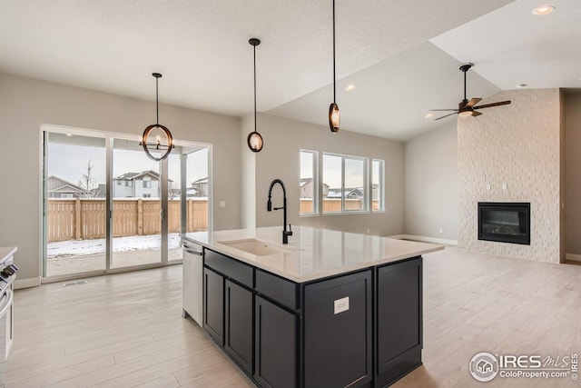 kitchen with lofted ceiling, a center island with sink, sink, stainless steel dishwasher, and a fireplace