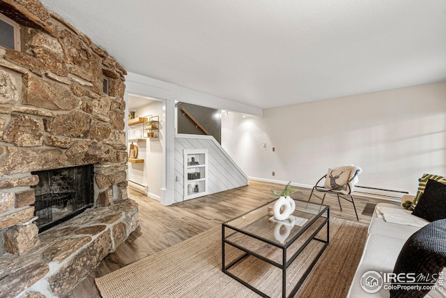 living room featuring a fireplace, a baseboard heating unit, and wood-type flooring