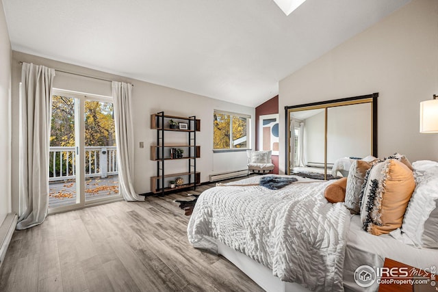 bedroom featuring baseboard heating, a closet, light hardwood / wood-style floors, vaulted ceiling with skylight, and access to outside