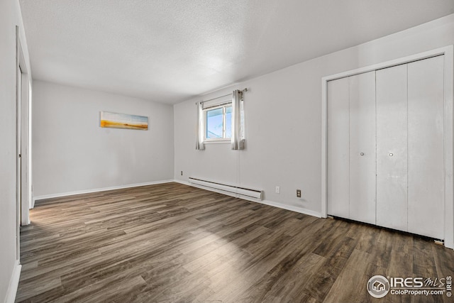 unfurnished bedroom featuring dark hardwood / wood-style flooring, a closet, baseboard heating, and a textured ceiling