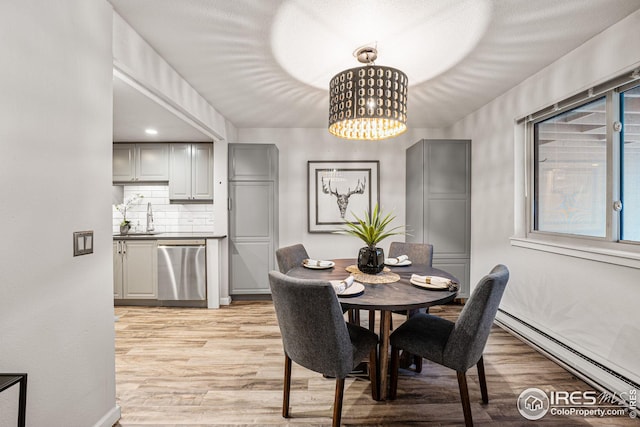 dining space featuring sink, a baseboard heating unit, a chandelier, and light hardwood / wood-style floors