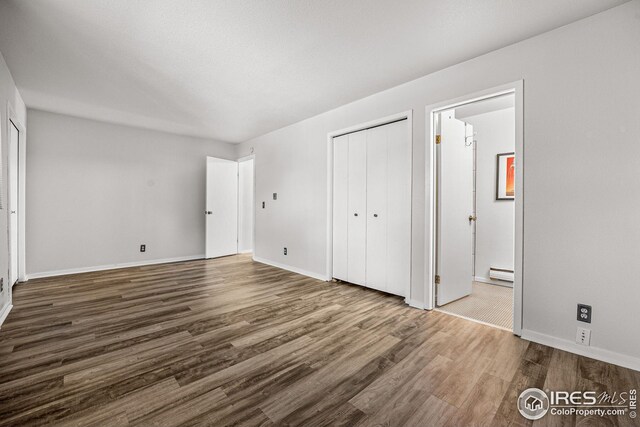 unfurnished bedroom with a baseboard radiator, a closet, ensuite bath, and wood-type flooring