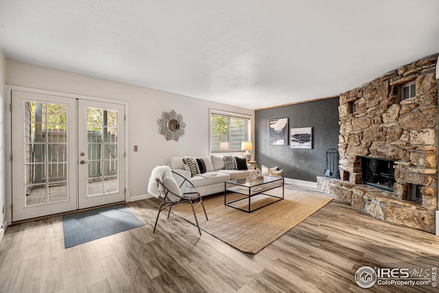 living room featuring french doors, wood-type flooring, a fireplace, and a healthy amount of sunlight