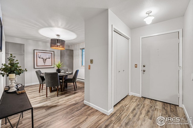 entrance foyer with a textured ceiling, a chandelier, a baseboard radiator, and wood-type flooring