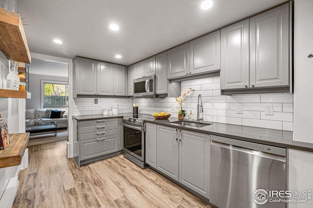 kitchen featuring gray cabinets, stainless steel appliances, light wood-type flooring, sink, and backsplash