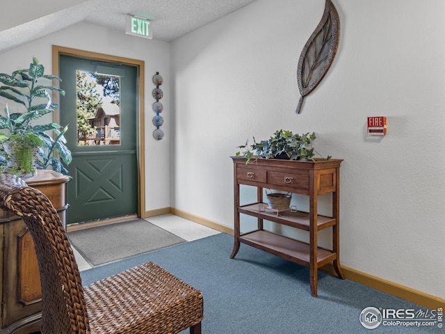 entryway with a textured ceiling, light colored carpet, and lofted ceiling